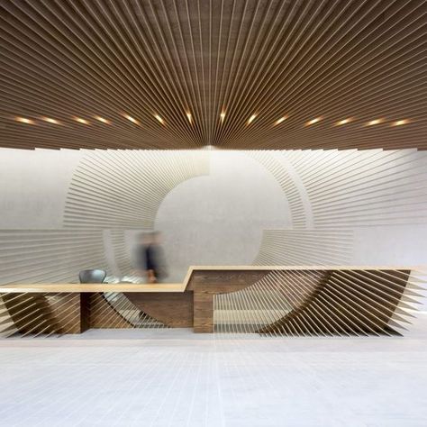 Bespoke Design for a High-End Reception Area. This installation showcases an exceptional design, incorporating wooden panels strategically aligned to create a unique graphic play. The central desk, with its sculptural lines and precise cutouts, seamlessly blends with the wall patterns and ceiling, offering an impressive visual continuity. The work on geometric shapes and materials reflects an advanced mastery of assembly and finishing techniques, ensuring a structure that is both elegant and durable. Integrated lighting highlights the architectural details, reinforcing a professional and refined atmosphere.