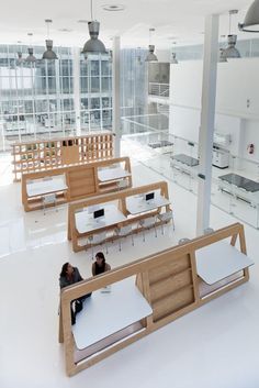 Bespoke Design for a Collaborative Study Library This design emphasizes an arrangement tailored to enhance both efficiency and comfort in a collaborative learning setting. The light wood modules delineate individual and shared spaces, fostering a seamless combination of group work and solitary study. The layout focuses on natural light, with open volumes and light materials contributing to an atmosphere that supports concentration. Each desk comes with practical shelving and dividers, striking a balance between privacy and interaction.