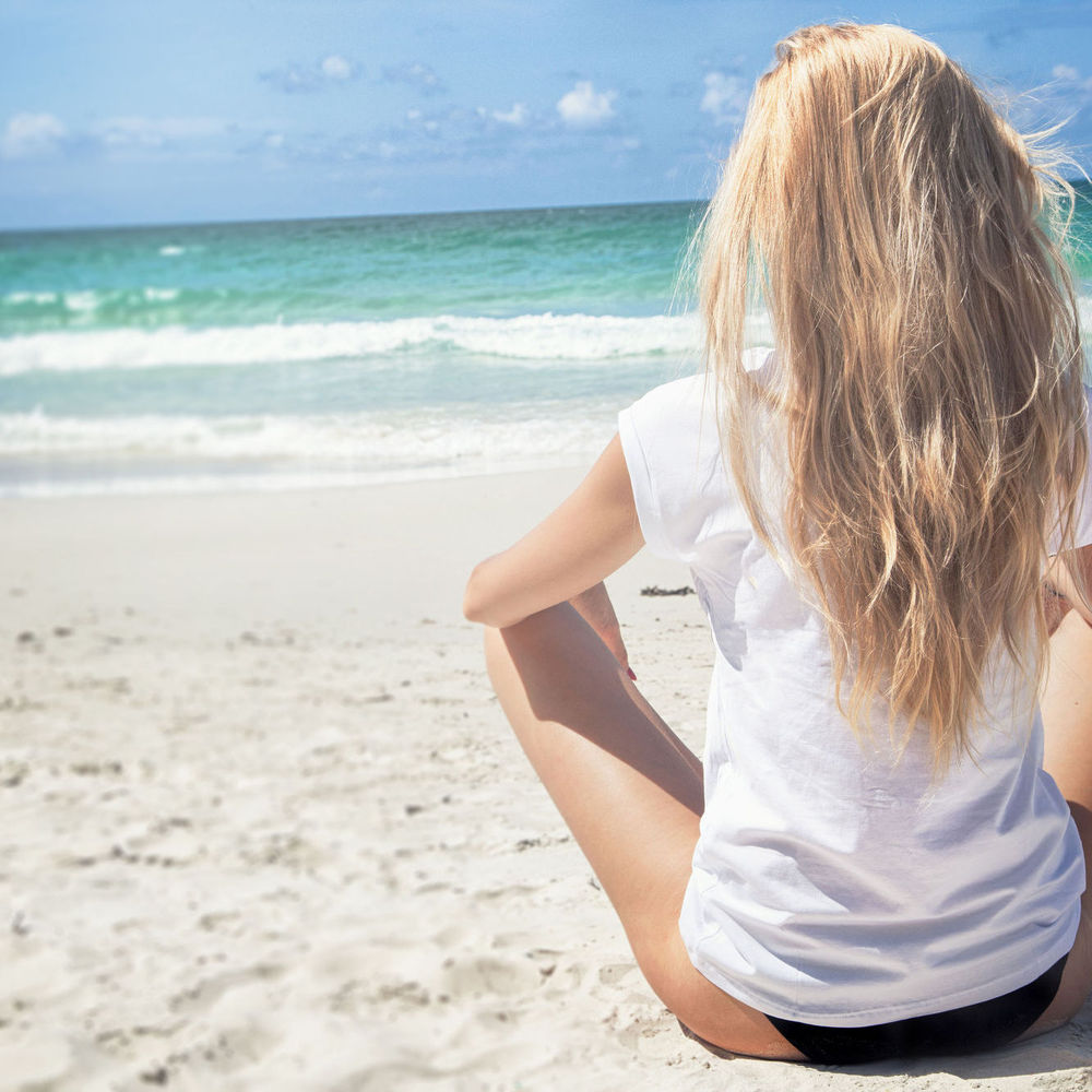 Девушка на пляже спиной читает книгу