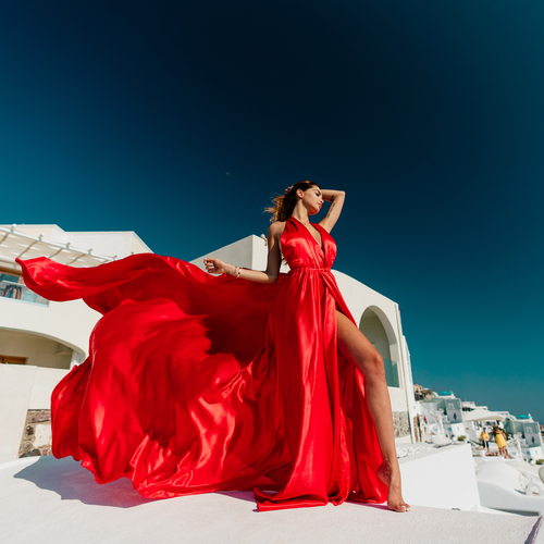 Woman in a red flying dress with a long flowing train on a white rooftop in Santorini