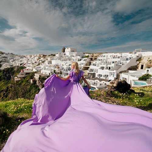 Woman in a lilac flying dress, the train spread over a hillside above a Santorini village