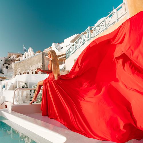 Woman in a scarlet flying dress beside a pool, the long train draped over the edge, Santorini