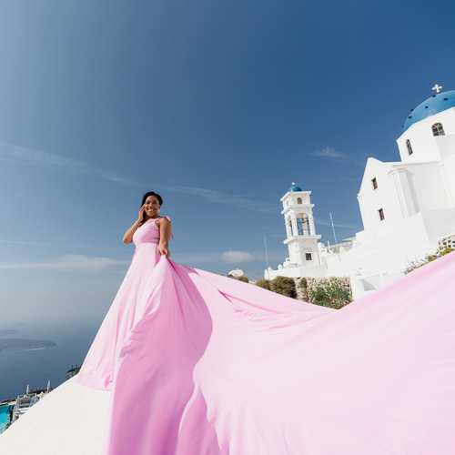 Woman in a pale rose flying dress with a long train on a white terrace in Santorini