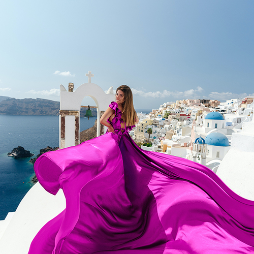 Woman in a fuchsia ruffled flying dress with the white village and blue domes of Santorini behind