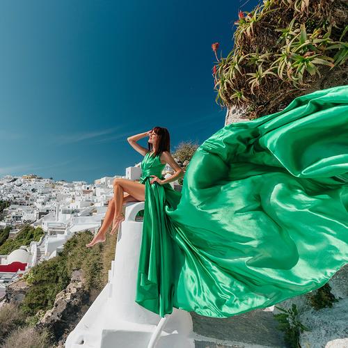Woman in an emerald green flying dress on a white staircase, the train billowing in the wind in Santorini