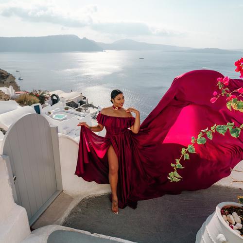 Woman in a burgundy off-the-shoulder ruffled flying dress beside bougainvillea in Santorini