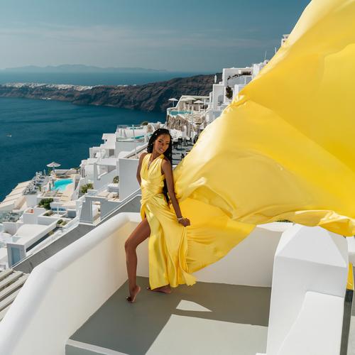 Woman in a yellow satin flying dress on a white terrace above the Santorini caldera
