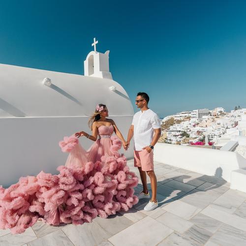 Couple beside a white chapel in Santorini, the woman in a voluminous pink tiered ruffle dress