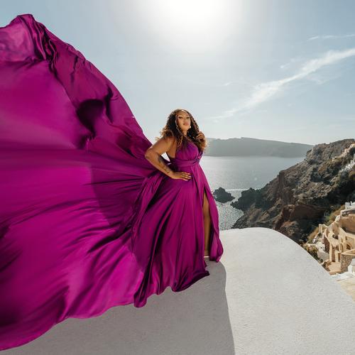 Woman in a fuchsia flying dress, the train lifted by the wind against the Santorini sky