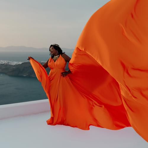 Woman in an orange flying dress, the train billowing over the sea in Santorini