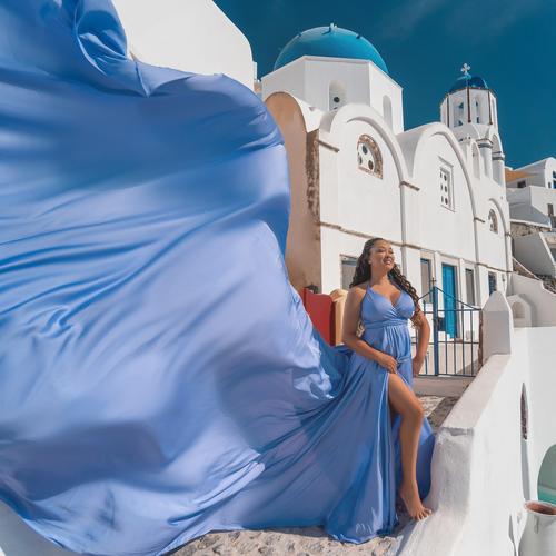 Woman in a lavender flying dress with blue-domed churches behind her in Santorini