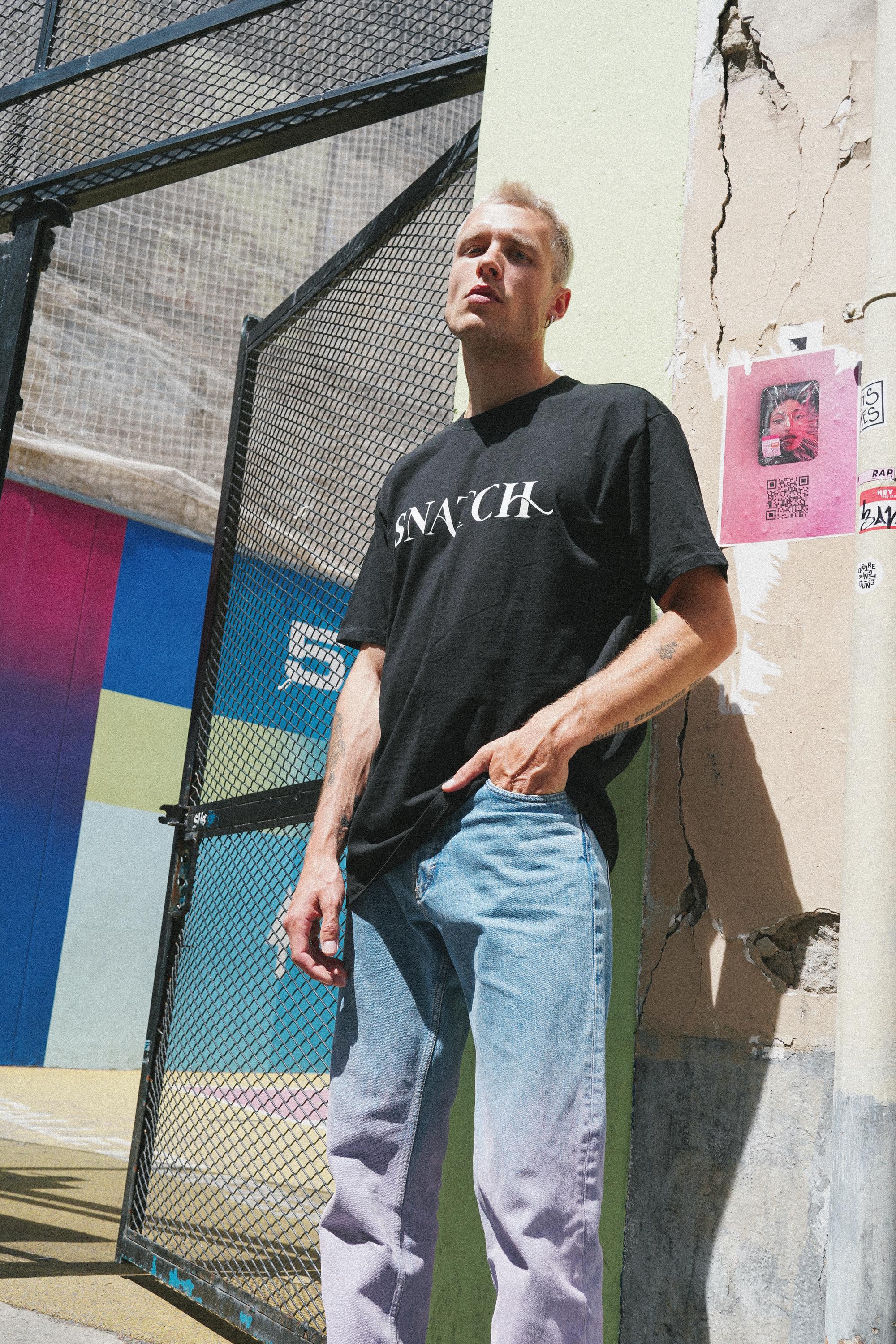 Male model showcasing SNATCH streetwear in front of graffiti wall by Paris street style fashion photographer