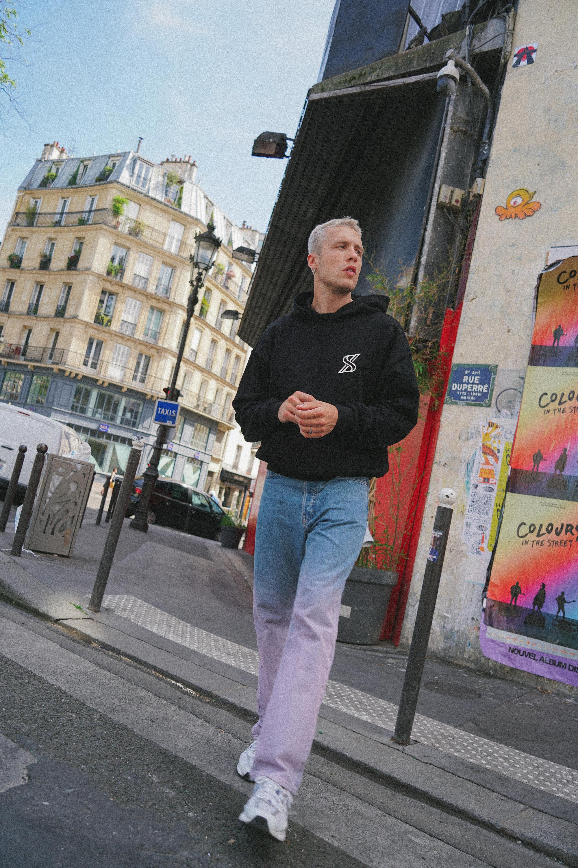 Male model posing with SNATCH hoodie against graffiti backdrop in Pigalle during street style shoot in Paris